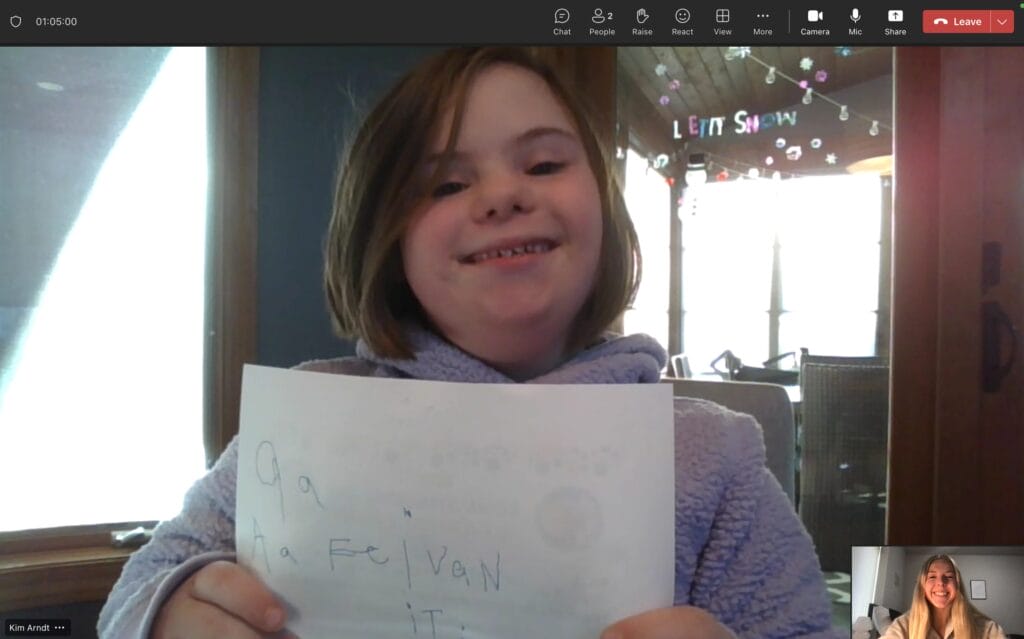 Young tutoring student with Down syndrome  holding a piece of paper and smiling during virtual tutoring